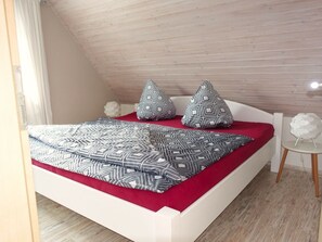 A bedroom with a sloped ceiling, a bed with patterned bedding, and a small white side table. - Holiday Apartment With 2 Bedrooms (Kappeln)