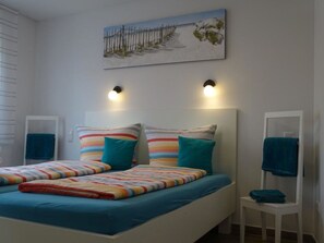 A bedroom with a bed, two bedside tables, a wall-mounted painting, and two wall-mounted lights. - Holiday Apartment With 2 Bedrooms (Norden)