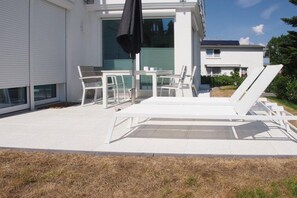 A modern outdoor patio with white furniture, including a table and chairs, and a sun lounger. - Timmare IV Fritz Cabin (Timmendorfer Strand)