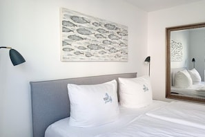 A hotel room with a bed, two pillows, a wall-mounted artwork, a mirror, and two bedside lamps. - Timmare IV Fritz Cabin (Timmendorfer Strand)