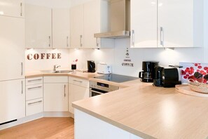 A modern kitchen with white cabinetry, a built-in stove, a coffee maker, and a basket of fruit. - House by the sea, Apartment 14 (Timmendorfer Strand)