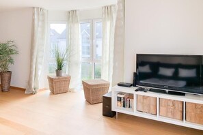 A living room with a flat-screen TV, wicker furniture, and a large window. - House by the sea, Apartment 14 (Timmendorfer Strand)