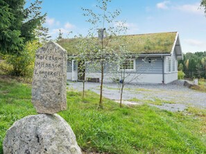 A stone marker with inscriptions, a house with a sloped roof, and a grassy area with trees. - Backa Gård by Interhome (Lur)