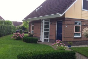 A two-story house with a brick facade, a dark roof, and a small front garden with pink flowers. - Holiday home Holland North (Medemblik)