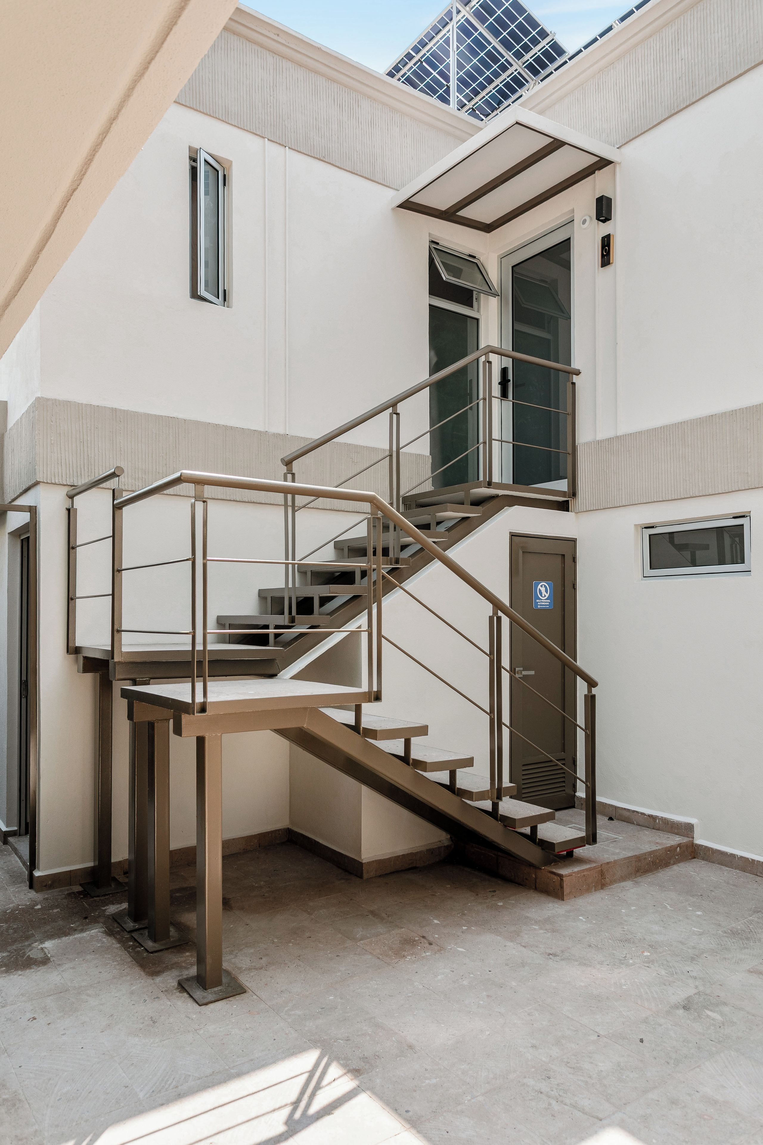 Una escalera exterior de varios niveles con barandillas de metal, que lleva a una puerta con un ventanal.
