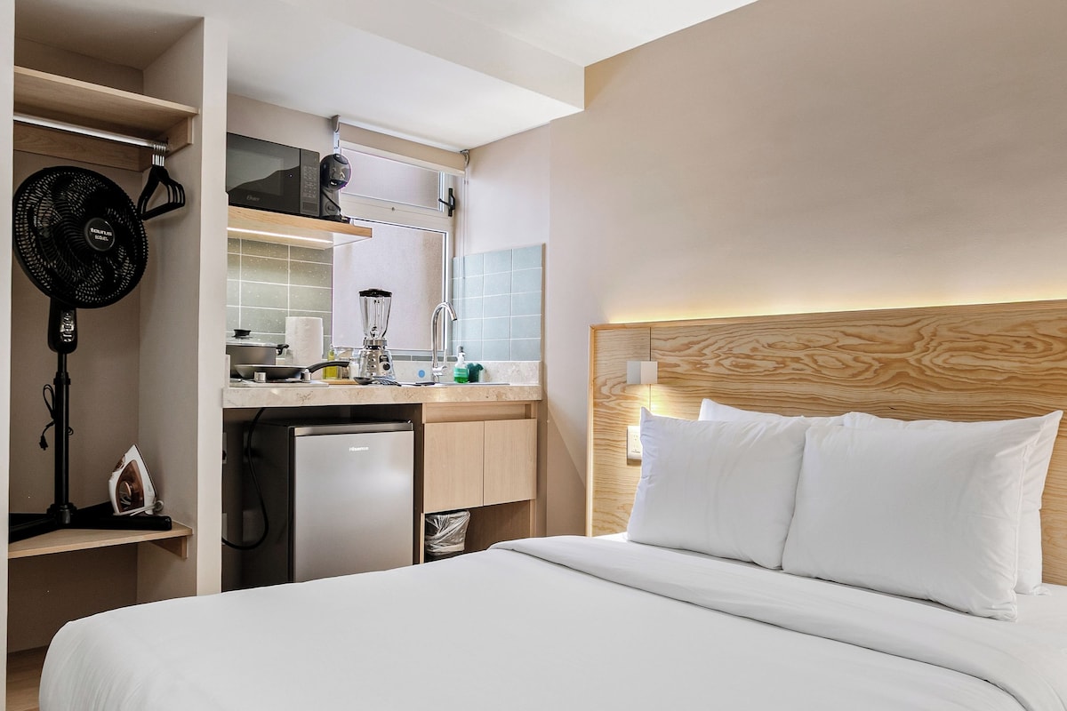 Una habitación de hotel con una cama grande, una kitchenette, un ventilador de techo y un cabecero de madera.