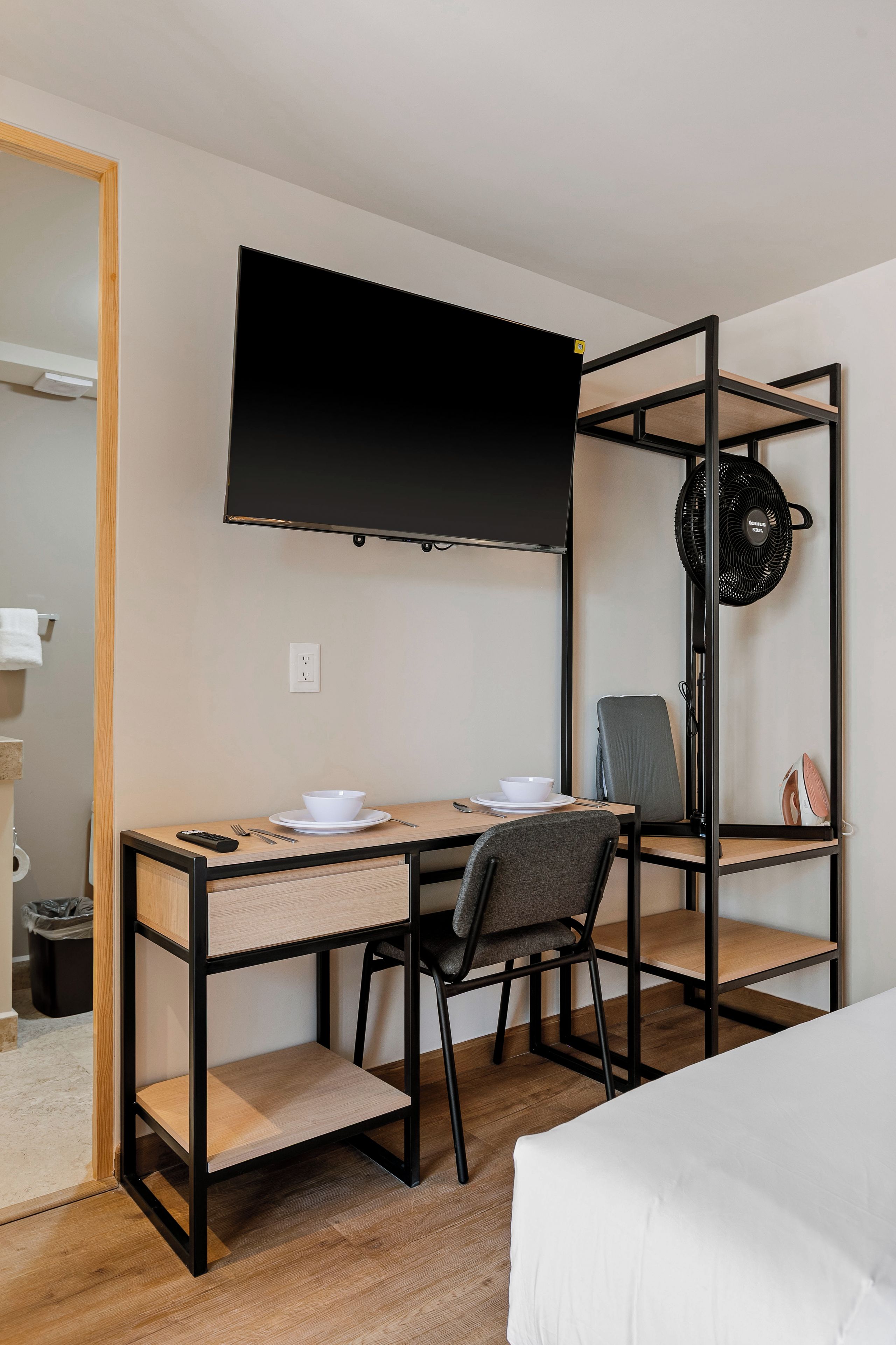 Una habitación de hotel con una cama, un escritorio con silla, un televisor y un ventilador.