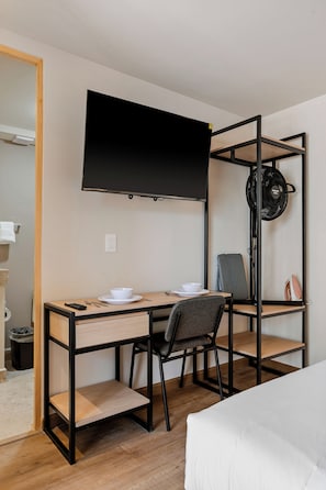 Una habitación de hotel con una cama, un escritorio con silla, un televisor y un ventilador.