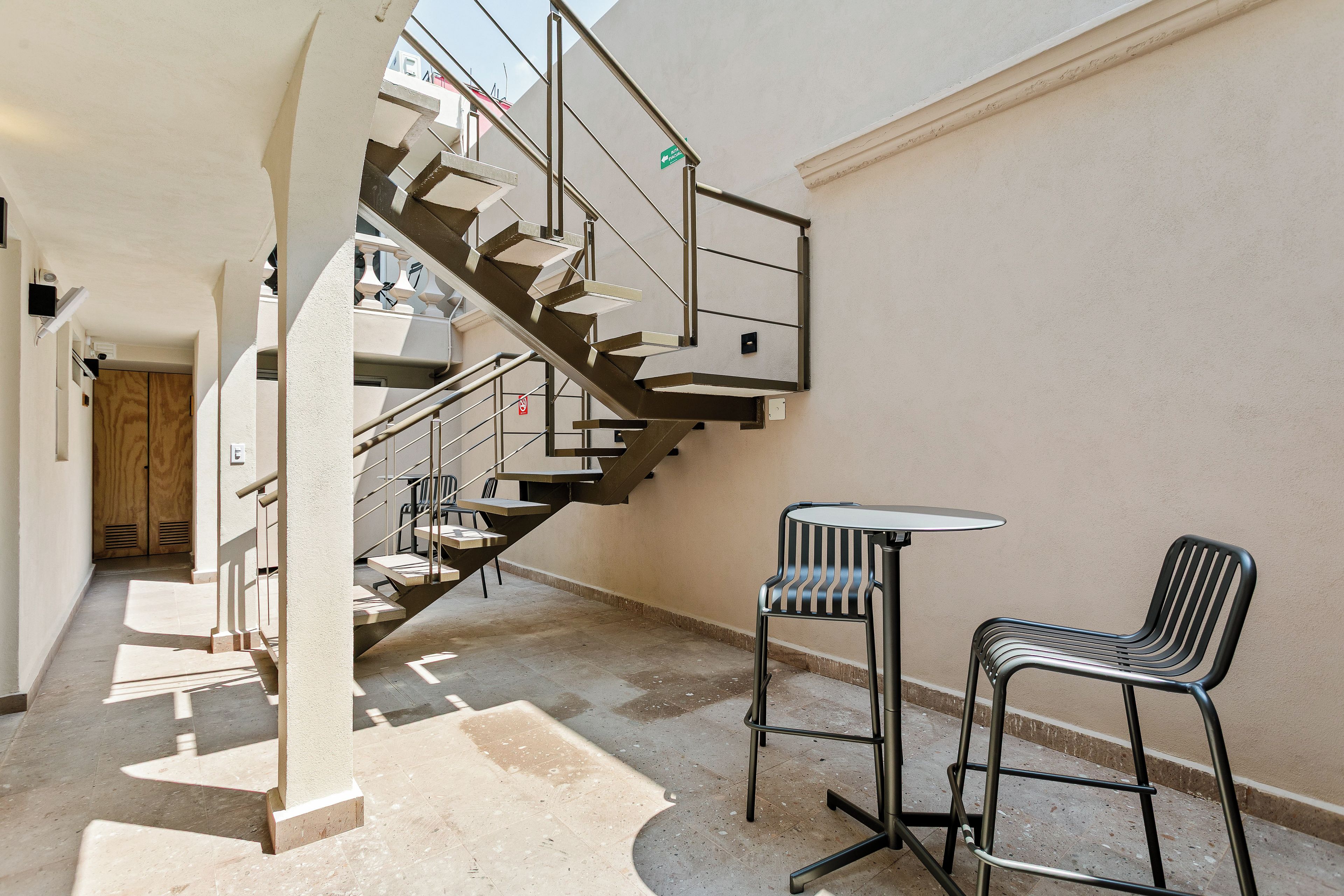 A staircase leading to an upper floor, a small outdoor seating area with two chairs and a table, and a door with a 'No Entry' sign.