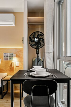 Un comedor moderno con una mesa preparada para dos, una silla negra y un ventilador de pie.