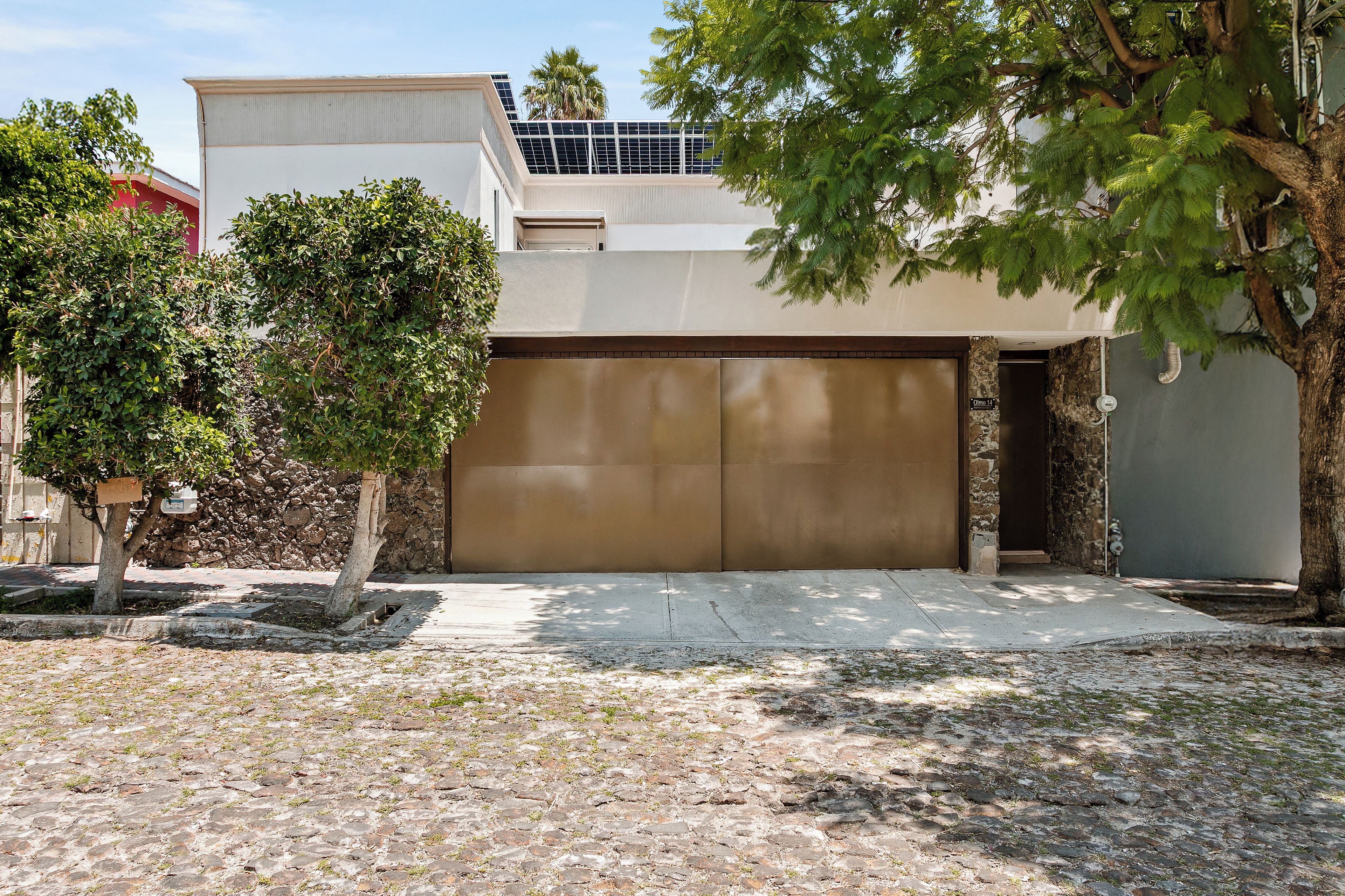A residential garage with a brown door, a stone wall, and a tree in the foreground.