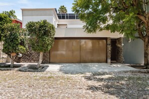 Un garaje residencial con una puerta marrón, un muro de piedra y un árbol en primer plano.