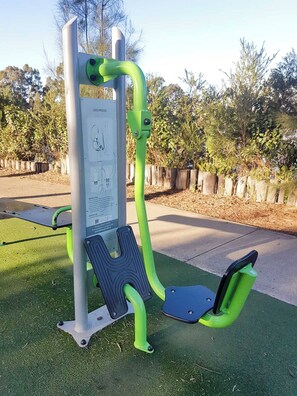 An outdoor exercise station with a leg press and a pull-up bar, surrounded by a wooden fence and trees. - The Wattle House - Your Home Away from Home (Wattle Grove)