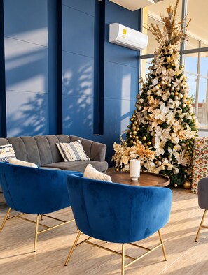 Ein modernes Wohnzimmer mit einem blauen Sofa, zwei blauen Sesseln, einem Couchtisch und einem dekorativen Weihnachtsbaum.