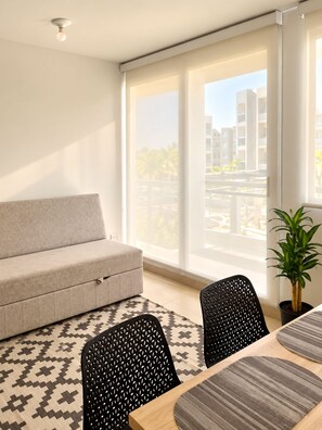 A modern living room with a sofa, two chairs, a dining table with a rug, a potted plant, and large windows with a view of buildings. - Experience Cartagena History Caribbean Flavors and Relaxation in Serena del Mar (Cartagena Province)