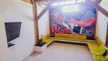A room with a sloped ceiling, a mural, a sofa, a television, and a small table with a plant.