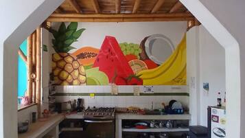 A kitchen with a wooden ceiling, a colorful fruit mural, and various kitchen appliances.
