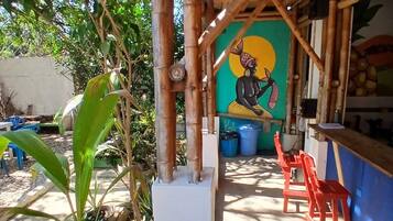 A covered outdoor area with a mural, potted plants, and red chairs.