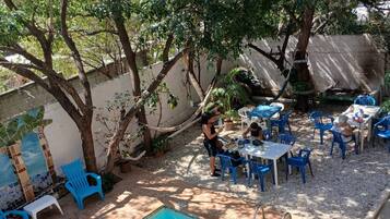 A swimming pool with blue chairs and tables, surrounded by trees and a tiled wall.