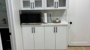 A kitchen with white cabinets, a microwave, and a basket with a plant.