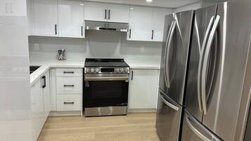 A modern kitchen with white cabinets, stainless steel appliances, and a wooden floor.