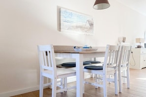 A dining area with a white table and chairs, a painting on the wall, and a lamp. - Holiday home with 3 bedrooms (Timmendorfer Strand \/ Niendorf)