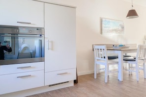 A modern kitchen with white cabinetry, a built-in oven, and a dining area with a table and chairs. - Holiday home with 3 bedrooms (Timmendorfer Strand \/ Niendorf)