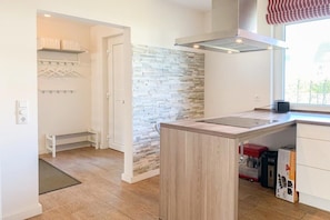 A modern kitchen with a central island, a stone accent wall, and a window providing natural light. - Holiday home with 3 bedrooms (Timmendorfer Strand \/ Niendorf)
