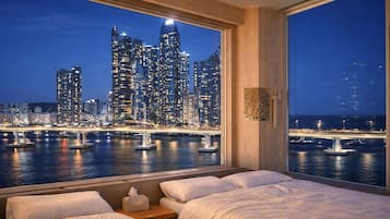 A hotel room with a large window overlooking a city skyline at night.