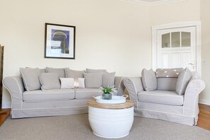 A living room with a beige sectional sofa, a round coffee table with a plant, and a framed picture on the wall. - Villa Démory Apartment 22 (Timmendorfer Strand)