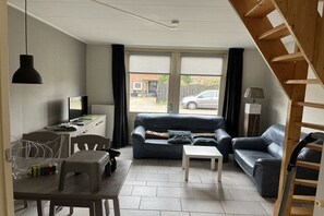 A living room with a sofa, a coffee table, a TV, and a staircase. - Holiday apartment in Petten with Wi-Fi (Petten)