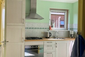 A kitchen with a gas stove, oven, stainless steel range hood, and a window with a view of a brick building. - Holiday apartment in Petten with Wi-Fi (Petten)