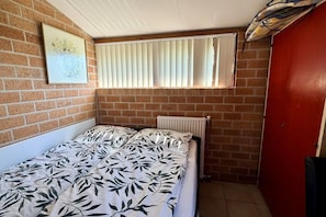 A small room with a bed, a radiator, a window with blinds, and a red door. - Holiday home in Schoorl with swimming pool (Schoorl)