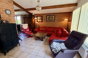 A living room with a red sofa, a black armchair, a wooden coffee table, and a black cabinet. - Holiday home in Schoorl with swimming pool (Schoorl)