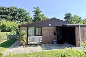 A single-story house with a brick exterior, a wooden bench, a gravel driveway, and a black garage door. - Holiday home in Schoorl with swimming pool (Schoorl)