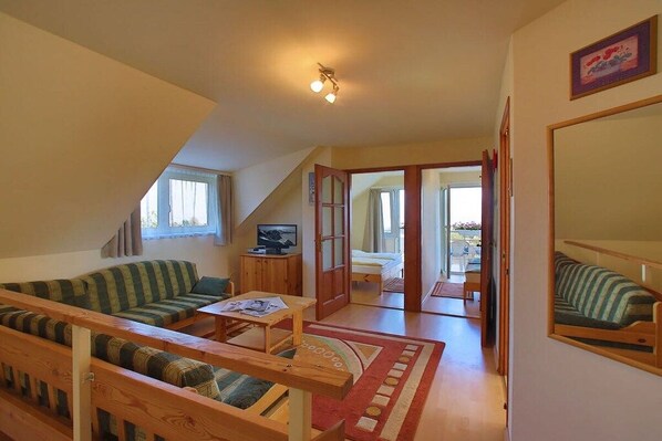A cozy room with a sofa, a small table, and a bed. There is a window and a door leading to another room.