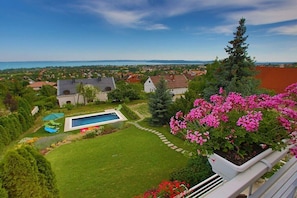 A residential property with a swimming pool, a well-maintained lawn, and a view of a body of water and distant landscape. - Villa in Balatonfüred with swimming pool (Balatonfüred)