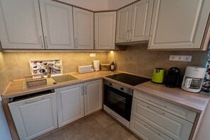 Una cocina con armarios blancos, una encimera, un fregadero, un horno y una cafetera.