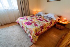 A bedroom with a floral bedspread, a bedside table with a lamp, and a wooden floor.