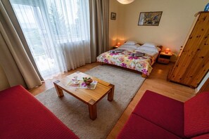 Un dormitorio con cama, mesitas de noche, un armario de madera, una ventana con cortinas y un sofá rojo.