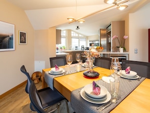 A dining area with a wooden table set for four, a vase with flowers, and a kitchen in the background. - Penthouse Villa Gudrun With Private Sauna (Binz)