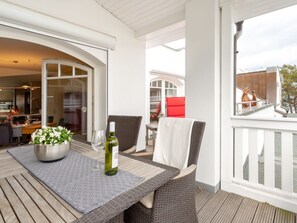 A covered outdoor dining area with wicker furniture, a table with a patterned table runner, and a bottle of wine. - Penthouse Villa Gudrun With Private Sauna (Binz)