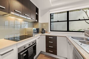 A modern kitchen with a stove, microwave, and sink. - Spacious 3-Level Windsor Townhouse | 2 Carparks (Brisbane)