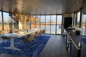 A modern kitchen with a large island, dining area with chairs, and hanging pendant lights. - Houseboat with 3 bedrooms (Oostknollendam)