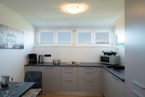 A modern kitchen with a dining area, featuring cabinets, a microwave, and a coffee maker. - Melanie's Guesthouse (Kaltern)