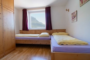 A small room with two wooden beds, a window with curtains, and a wooden wardrobe. - Melanie's Guesthouse (Kaltern)