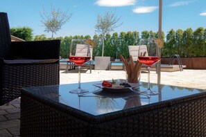 An outdoor seating area with wicker furniture, a glass table, and two glasses of red wine. - Melanie's Guesthouse (Kaltern)