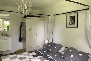 A bedroom with a bed, a wardrobe, a chandelier, a framed picture, and a window. - Holiday home with 1 bedroom (Oostkapelle)