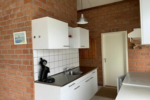 A kitchen with white cabinets, a coffee maker, and a brick wall. - Holiday home with 1 bedroom (Burgerbrug)