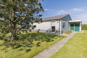 A single-story building with a stone facade, a garage with green doors, and a well-maintained lawn. - Holiday home with 1 bedroom (Burgerbrug)